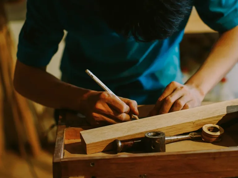 Hands marking a piece of wood with a pencil on a workbench.